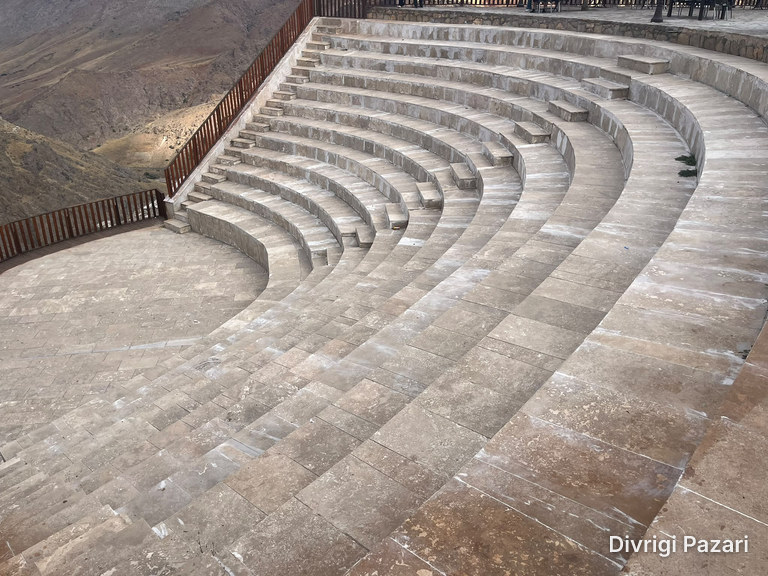 Curved stone seating steps seen from above, with a wooden railing and the canyon slope beyond