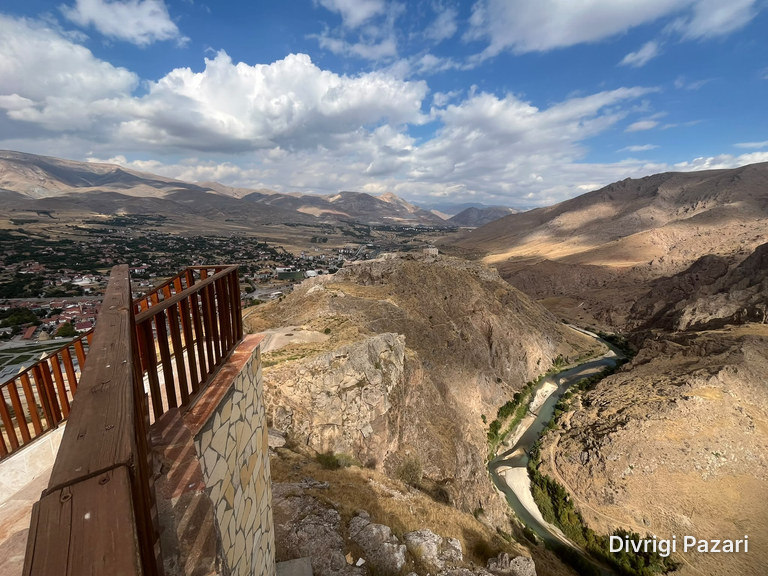 Beyond the terrace's wooden railing: Divriği's roofs, stone walls along a rocky ridge and the Çaltı winding through the canyon