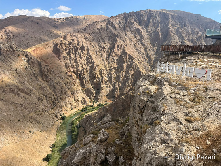 The Çaltı flowing at the bottom of a deep canyon; on the right, a letter sign on the rocks, the wooden walkway and the glass terrace