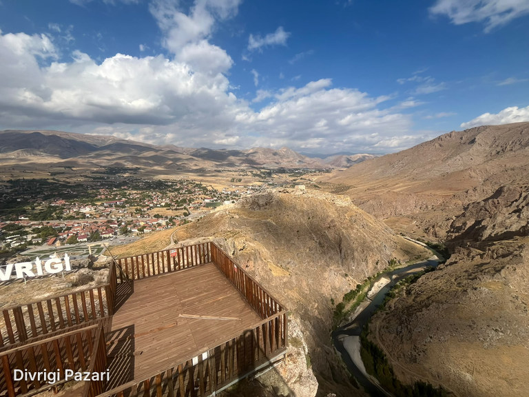 A wooden viewing deck on the rocks; beyond it the houses of Divriği, a rocky ridge and the Çaltı in the canyon