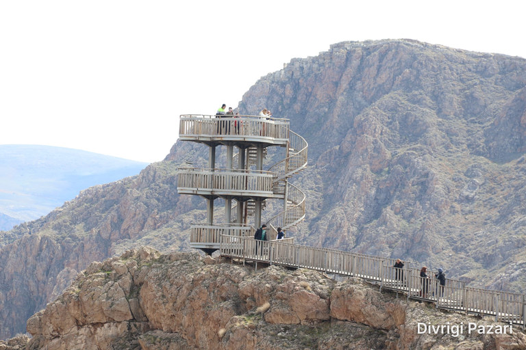 A wooden viewing tower with a spiral stair on a rocky hilltop, and visitors on the walkway