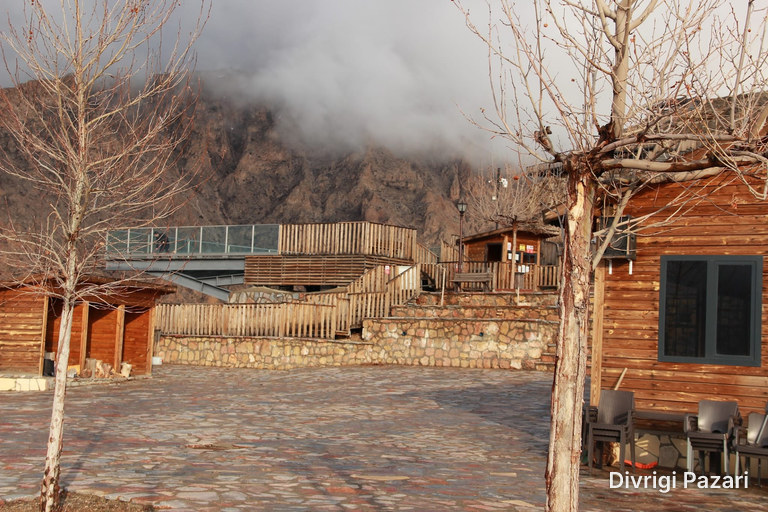 On a foggy day: bare trees, a stone-paved square and wooden buildings; a rocky mountain and the glass terrace behind