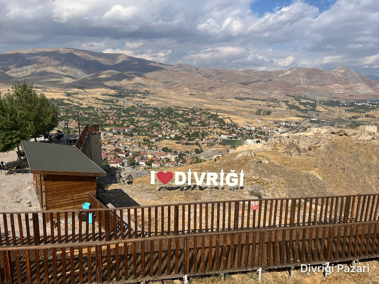 The heart-shaped Divriği sign, a wooden hut and railing; the houses of Divriği and the mountains behind