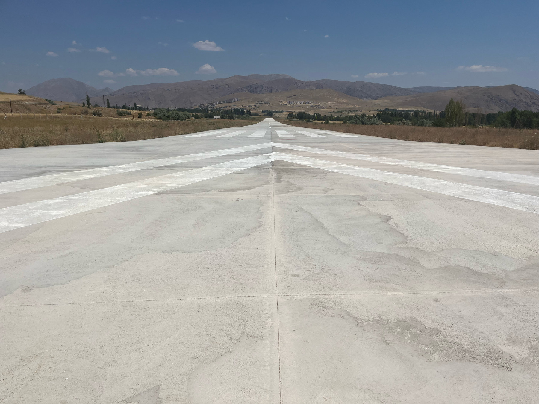 The concrete runway at Nuri Demirağ Air Campus: threshold markings and the centreline running towards the horizon, with the mountains and the town of Divriği behind