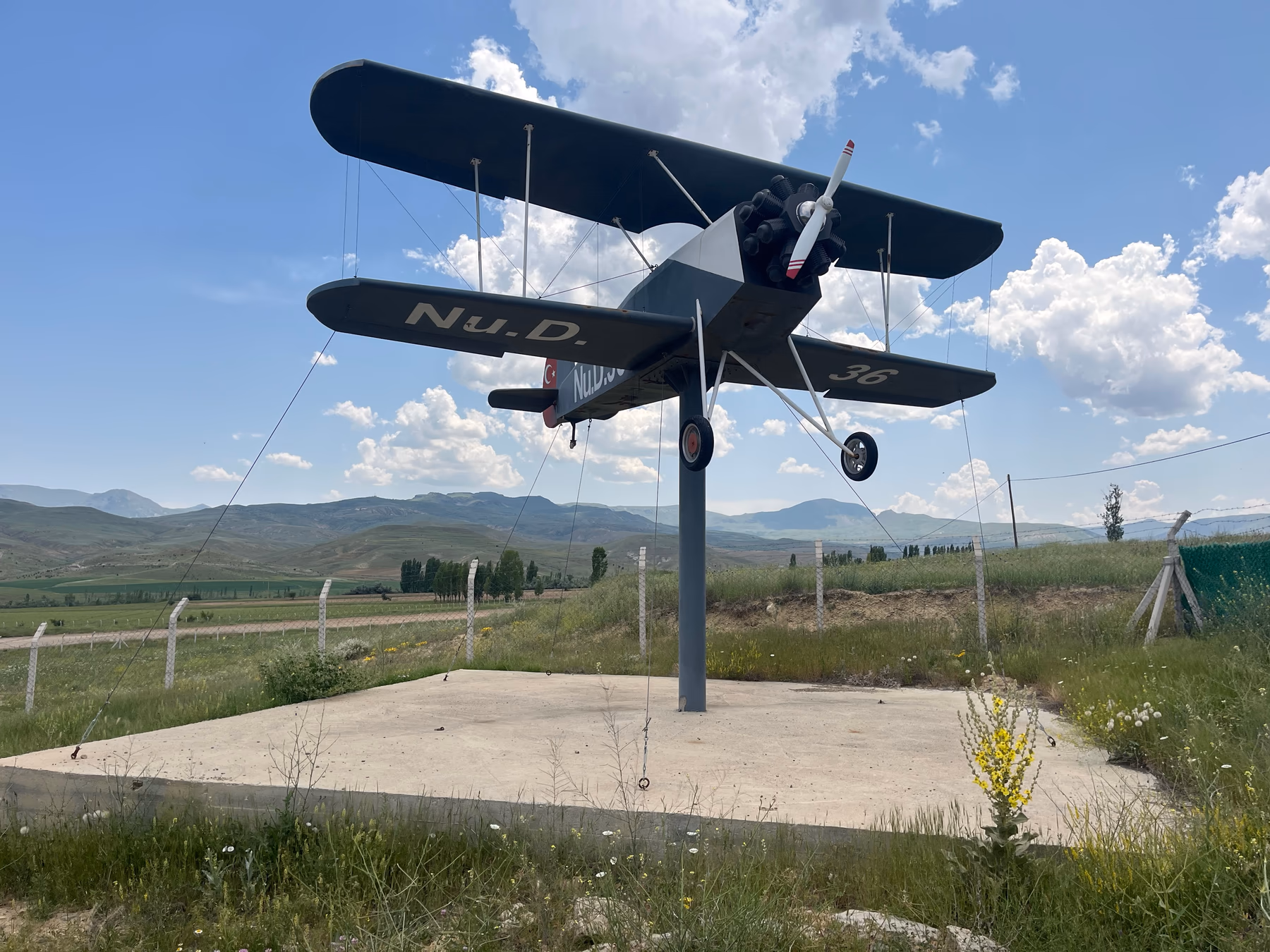 Aircraft monument bearing the Nu.D.36 name displayed outdoors with mountains around it